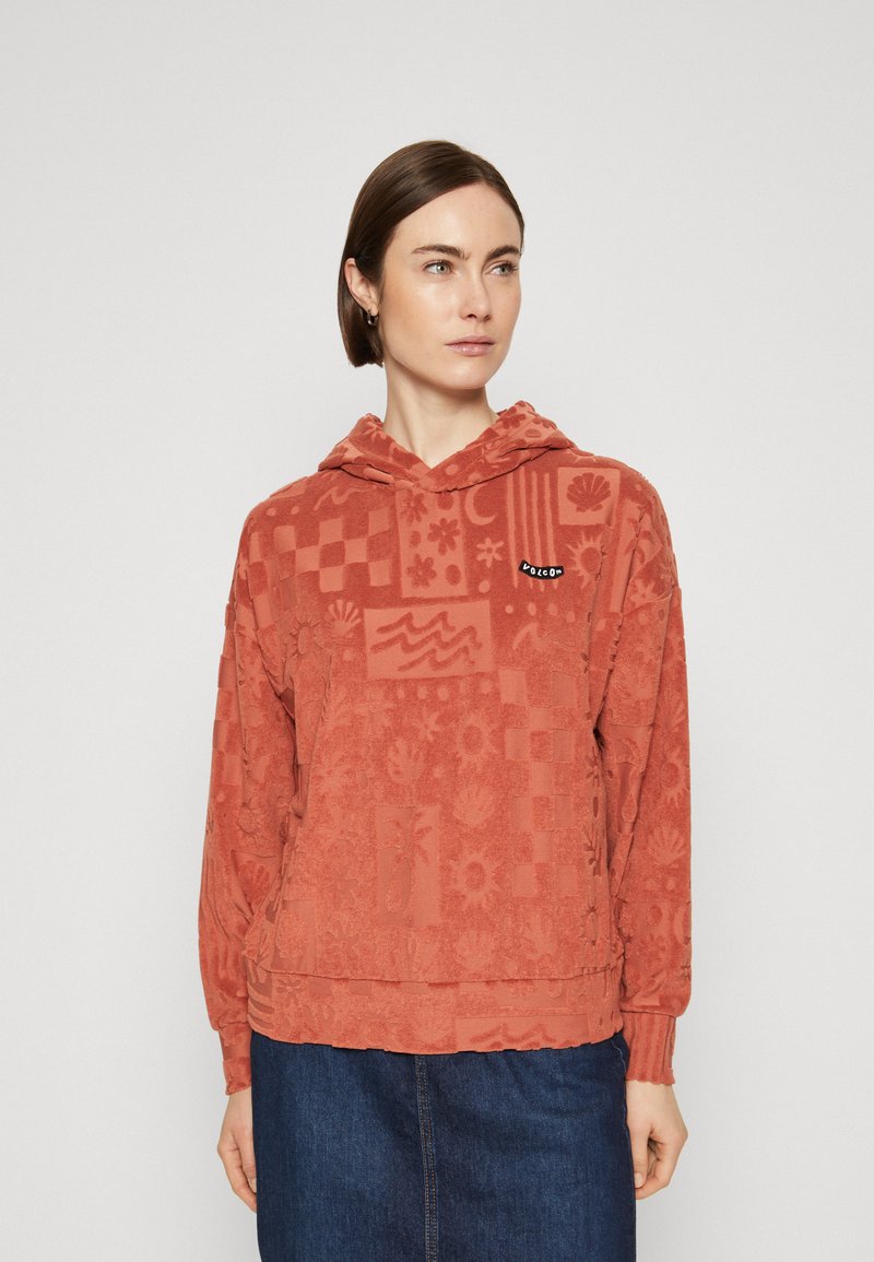 Sudadera de color óxido con un patrón texturizado de flores y formas geométricas. Incluye un bolsillo canguro en la parte frontal y capucha con cordón.