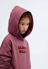 Vínová mikina s kapucí a přední kapsou, na které je červený nápis "CLUB DE BALLER". Měkká, strukturovaná tkanina s uvolněným střihem.