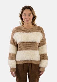 Maglione a righe marroni e crema con un motivo di maglia texturizzato, filato peloso e polsini a coste. Indossato con pantaloni marroni per creare un contrasto.