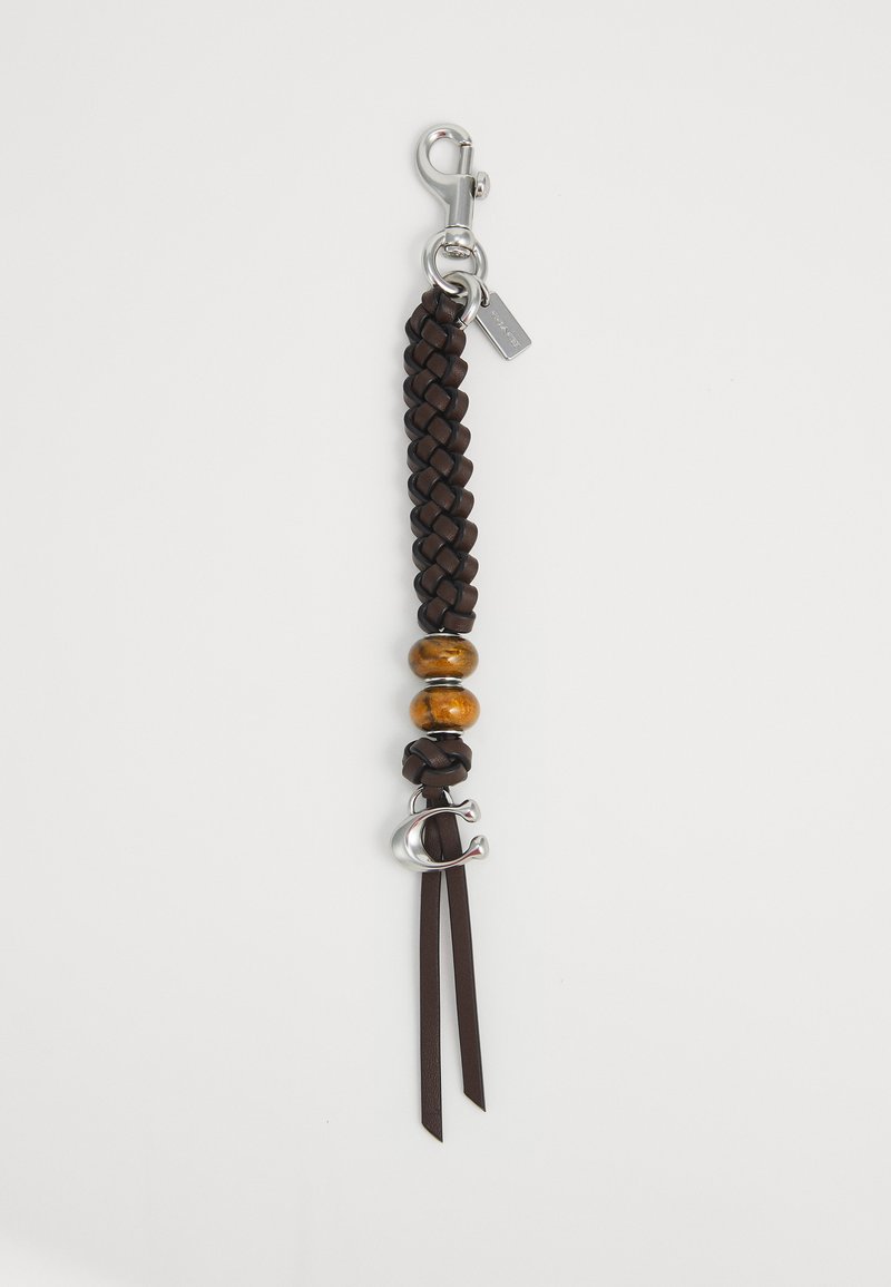 Rjav pleteni usnjen obesek za ključe z dvema lesenima kroglicama, srebrnim sponko in srebrnim obeskom v obliki črke "C" na belem ozadju.