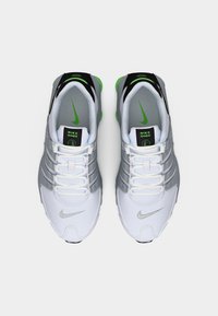 Αθλητικά παπούτσια Nike Shox σε λευκό και γκρι με πράσινες λεπτομέρειες. Διαθέτουν κομψό σχεδιασμό, υλικά με υφή και τέσσερις ορατές στήλες απορρόφησης κραδασμών.