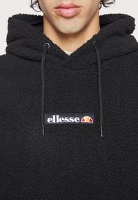 Felpa nera in pile con superficie testurizzata, dotata di cappuccio con coulisse e toppa del logo ricamata sul davanti in bianco e rosso su sfondo nero.