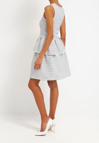 Pruhovaná peplum šaty v bílé a námořnické modři, s přiléhavým trupem a rozšířenou sukní; nošeny s bílými vysokými podpatky.