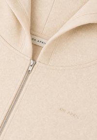 Sweat à capuche beige avec fermeture éclair en métal et texte "OH APRIL" brodé sur la partie avant de la poitrine.