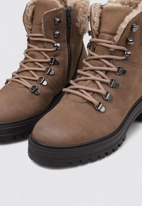 Braune, strukturierte Lederknöchelstiefel mit Kunstfellfutter, Schnürdesign, Metallösen und einer klobigen schwarzen Gummisohle.