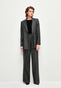Completo a due pezzi grigio scintillante composto da un blazer su misura e pantaloni a gamba larga, caratterizzato da un design strutturato e un tessuto testurizzato. Top nero sotto.
