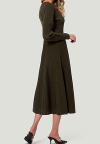 Robe longue côtelée vert olive avec des manches longues et une jupe évasée. Présente un corsage ajusté et un léger éclat pour la texture.