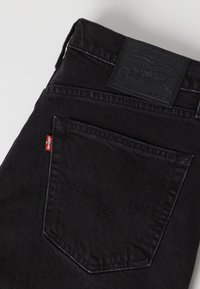 Μαύρα τζιν denim με πίσω τσέπη, κόκκινη ετικέτα Levi's και μαύρο δερμάτινο λογότυπο Levi's στη μέση.