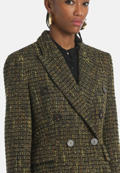 Double-breasted blazer made of textured tweed in dark green and yellow hues, featuring large brown buttons and a tailored fit.