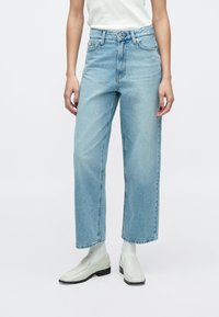 Világoskék farmernadrág, bő szárú, magas derekú, finoman kopott részletekkel, egyszerű fehér cipővel párosítva.