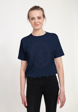T-shirt di cotone blu navy con una grande grafica scura di una bottiglia di Coke e testo. Maniche corte, vestibilità comoda e una texture liscia.