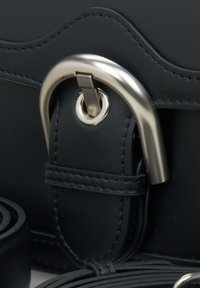 Zwarte leren handtas met een metallic zilveren gesp, een gestructureerd oppervlak en een gerolde schouderriem. Heeft gestikte accenten en een gebogen ontwerp.