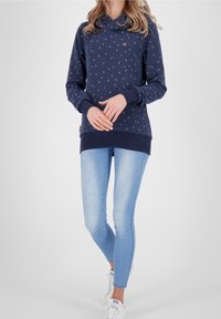Sudadera Navy con cuello de cowl, patrón floral disperso en azul claro, puños y dobladillo acanalados; combinada con jeans skinny azul claro y zapatillas blancas.