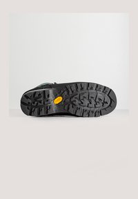 Zwarte rubberen zool met diepe noppen, voorzien van een verhoogd geel logo. Eenvoudig, getextureerd patroon voor grip. Ontworpen voor duurzaamheid en grip.
