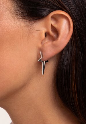 Silberne und schwarze geometrische Ohrringe in Sternform mit einem eleganten, modernen Design und glatter Metalloberfläche, die am Ohr getragen werden.