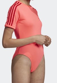 Neonrosa baddräkt med kort ärm och figurnära design, upprullade ärmar och tre röda ränder längs axlarna. Slätt, stretchigt material.