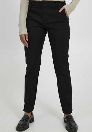 Černé kalhoty na míru z hladké tkaniny, se slim fit, bočními kapsami a plochým předním designem. Nosené s černými mokasíny.