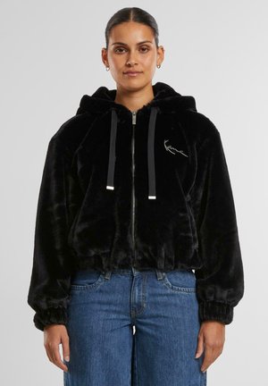 Svart cropped zip-up hettegenser laget av myk, plysj stoff. Har snorhette, ribbede mansjetter, og brodert logo på brystet.