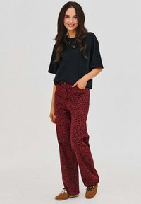 Čierne nadrozmerné tričko v kombinácii s červenými nohavicami s leopardím vzorom a vysokým pásom. Nohavice majú rovný strih a jemné detaily zadných vreciek.