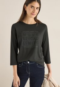 Schwarzes Langarm-T-Shirt mit Rundhalsausschnitt, verziert mit einem Textgrafik "MOVE BEYOND LIMITS" und "FREEDOM STARTS HERE" in einem strukturierten Design.