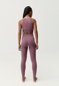 Lila sportos szett, amely egy testhez simuló, texturált mintájú tank toppból és magas derekú leggingsből áll. Simára finomított anyag, minimalista részletek láthatók.