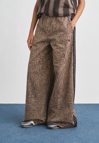 Wide-leg pants in a brown animal print with a textured pattern. Features an elastic waistband and black side stripes. Styled with gray shoes.