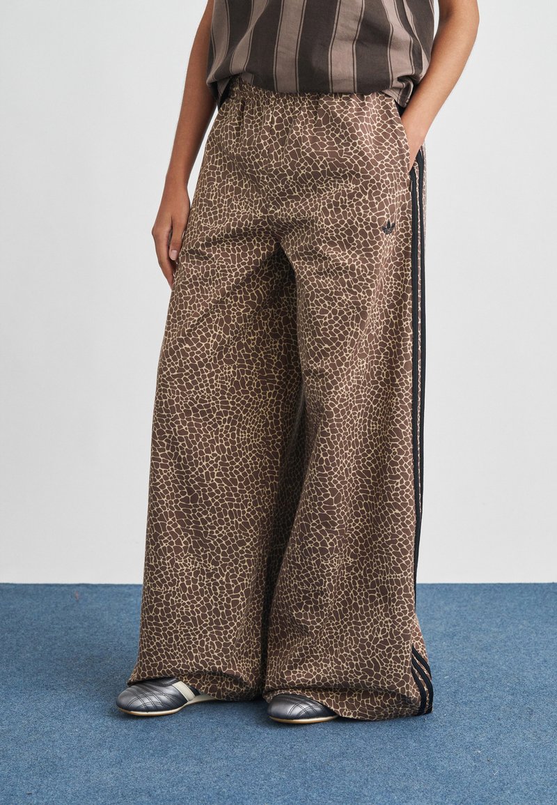 Wide-leg pants in a brown animal print with a textured pattern. Features an elastic waistband and black side stripes. Styled with gray shoes.