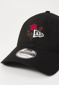Black adjustable baseball cap featuring red and green embroidered roses and a white logo. Fabric texture is smooth with a structured crown.