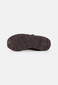 Suola di scarpa in gomma con un motivo ondulato, di colore marrone scuro, caratterizzata da piccoli segni a croce e macchie, con una texture liscia.