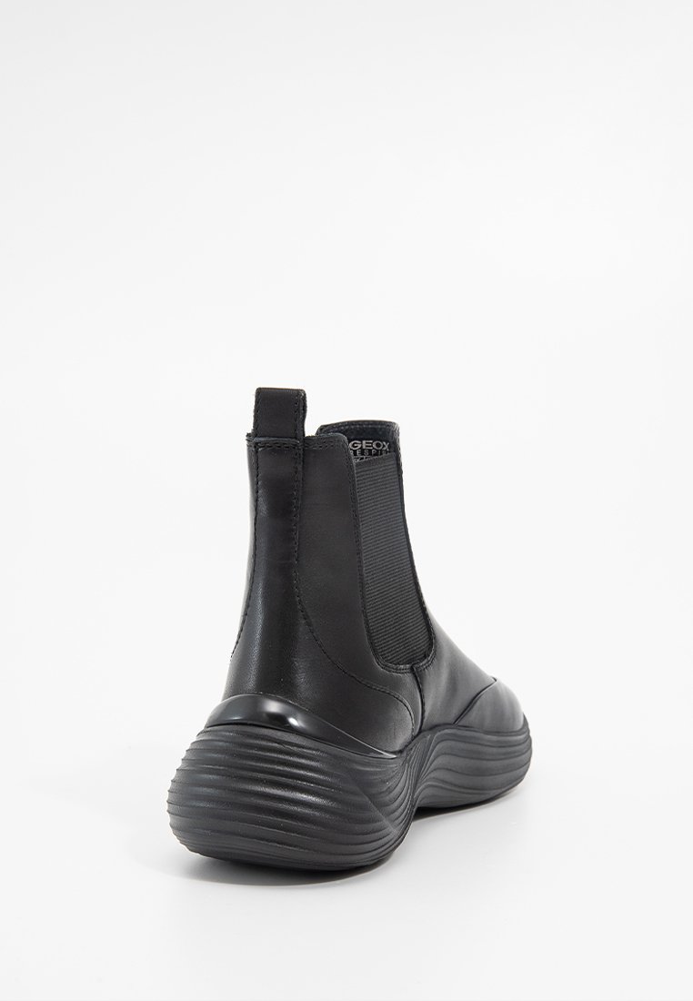 Botte noire à cheville avec semelle cannelée, panneau latéral élastique, languette au talon et logo subtil à l'arrière en haut, sur fond blanc.