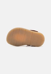 Brun mockaskoinötl med strukturerade mönster, med en gummibaserad beige sula. Diskreta spår och åsar förbättrar greppet och hållbarheten.