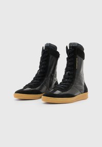 Sneaker alte nere in pelle e suede, con dettagli perforati, suola in gomma testurizzata e un audace marchio a contrasto sulla linguetta.