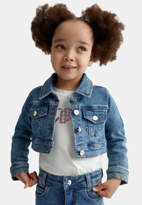 Giacca di jeans con un lavaggio azzurro chiaro, bottoni argento e tasche sul petto. Abbinata a una maglietta bianca con scritte rosa e jeans blu.