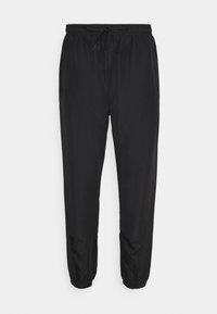 Zwarte joggingsbroek van lichtgewicht stof met een elastische tailleband, trekkoord en taps toelopende boorden. Beschikt over geaccentueerde texturen op de knieën.