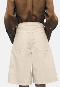 Shorts couleur crème, arrivant aux genoux, avec une coupe large et droite, comportant deux poches arrière et une taille plate.