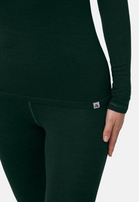 Groen, langermig shirt gecombineerd met bijpassende nauwsluitende legging. Beide gemaakt van zacht, gestructureerd materiaal. Label aan de zijkant vastgenaaid.