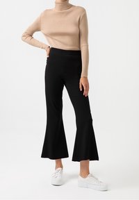 Béžový žebrovaný rolák v kombinaci s černými rozšířenými kalhotami a bílými teniskami. Oblečení má přiléhavý střih a hladkou texturu.