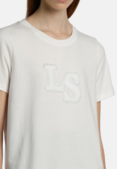 Balta kokvilnas T-krekls ar teksturētu izšūtu "LS" logotipu, kas ir tajā pašā krāsā. Īsas piedurknes un apaļa apkakle.