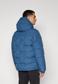 Chaqueta acolchada azul con capucha, con un diseño acolchado, puños elásticos y un ajuste relajado. El material parece brillante y suave.