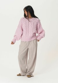 Pull en laine rose avec des motifs en relief, poignets côtelés et coupe décontractée, associé à un pantalon large beige clair et des chaussures marron.