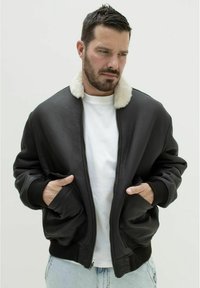 Sort læderbomberjakke med en fåreskindskrave, ribbede manchetter og to forlommer. Båret over en hvid T-shirt og lyse denim.