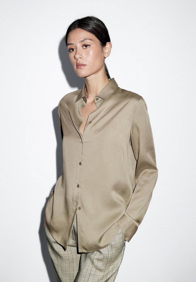 Beige satijnen overhemd met knopen en een losse pasvorm, voorzien van een kraag, lange mouwen en een subtiele glans. Gecombineerd met geruite broeken.