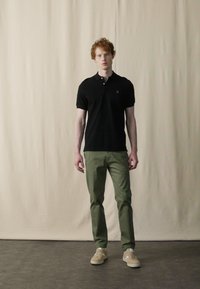 Camisa polo negra con cuello, pantalones verdes slim-fit y zapatillas beige. Diseño simple, estilo casual, colores sólidos en toda la indumentaria.