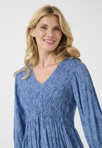 Abito blu con maniche lunghe, dotato di scollo a V, corpo testurizzato con dettagli arricciati e gonna fluida, realizzato in tessuto leggero.