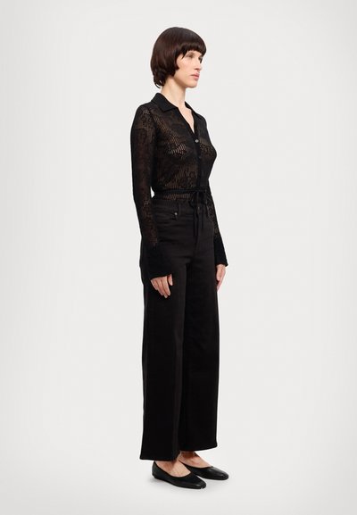 Maglietta nera, aderente, a maniche lunghe con un design trasparente e decorato; abbinata a pantaloni a vita alta e a gamba larga e a ballerine nere.