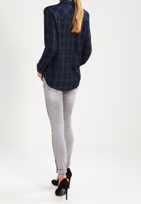 Chemise en flanelle à carreaux vert foncé et bleu marine à manches longues, associée à un jean slim gris clair et des chaussures à talons noirs.