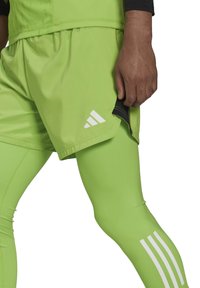 Neon groene sportshorts en legging, met witte drie-strepen branding, een lichtgewicht, gladde textuur en contraststiksels.
