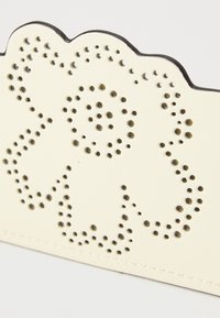 Portafoglio in pelle crema con un design floreale perforato e bordi scallopati, con dettagli in tono oro e cuciture.