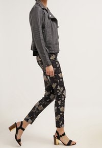 Chaqueta de cuero negra de estilo motociclista con detalles de cremallera, combinada con pantalones de estampado floral en tonos oscuros y sandalias negras con tacones cuadrados dorados.