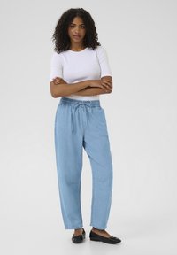 Lyseblå denimbukser med elastisk talje og snoretræk, featuring en afslappet pasform og sidelommer. Båret med en hvid tætsiddende top.